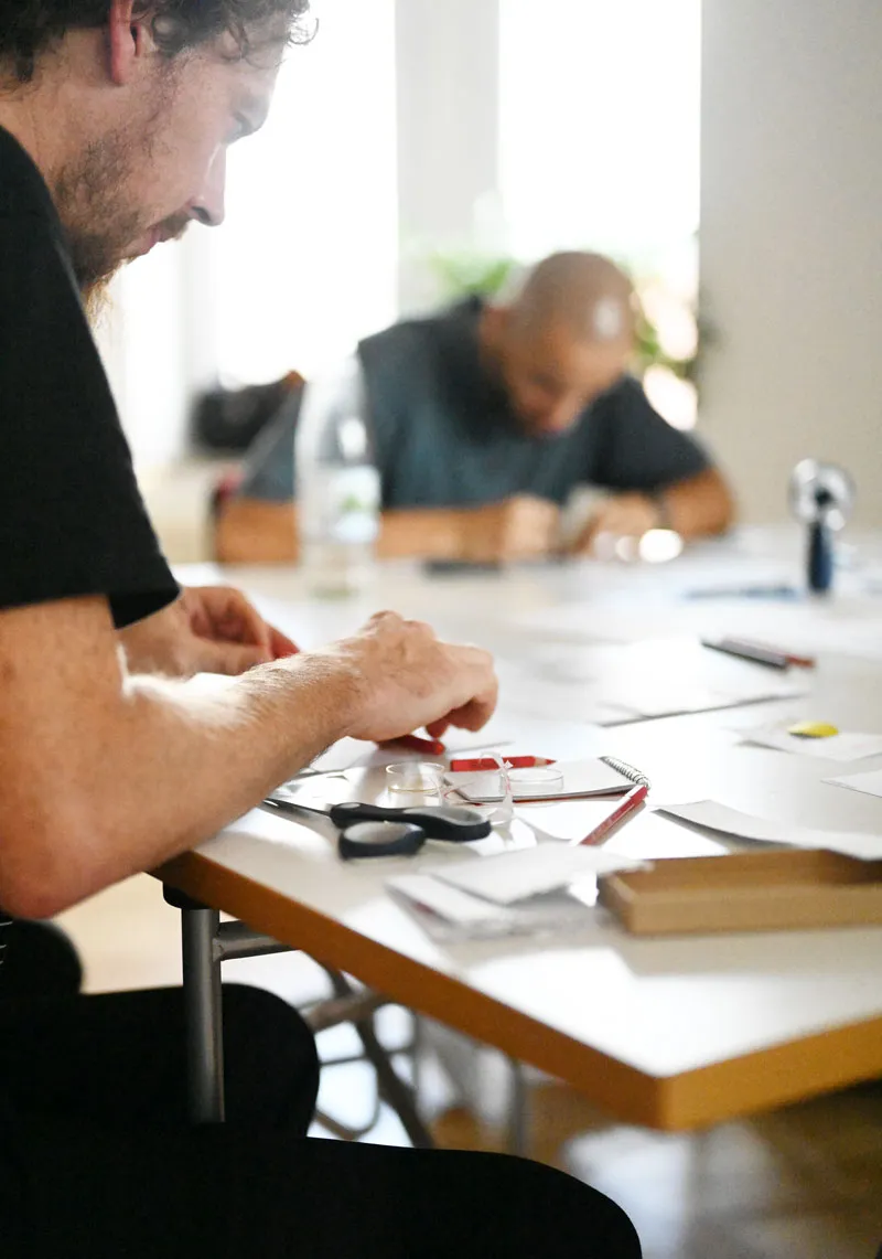 Workshop Impression: Menschen sitzen um einen Tisch und Arbeiten mit Stift und Schere